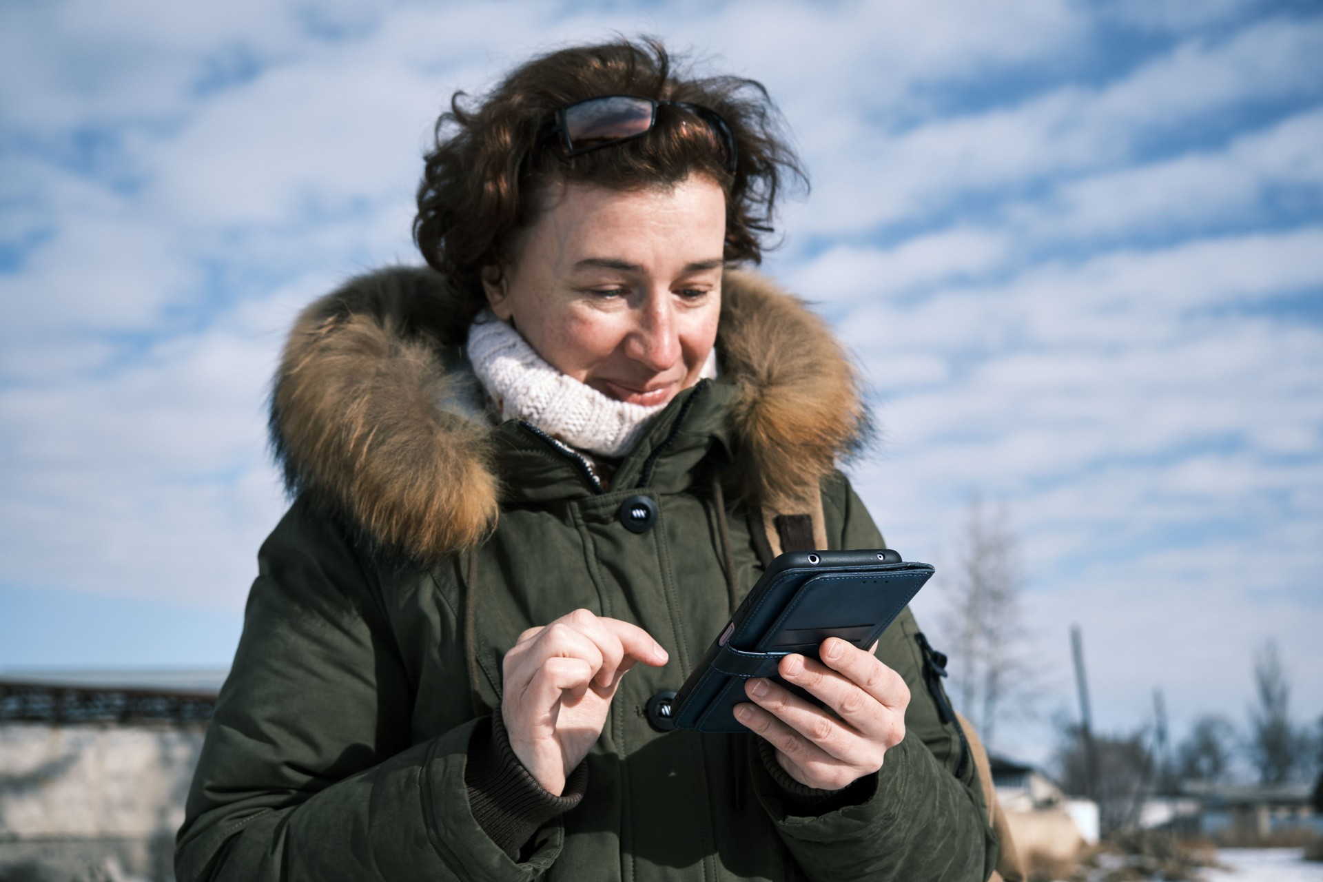 Woman wearing sunglasses is using phone on sunny winter town street